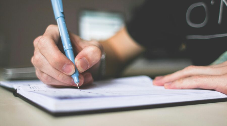 Close-up of hand writing in notebook using a blue pen, focus on creativity.
